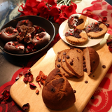 Baked goods on a wooden board with a red floral arrangement in the background