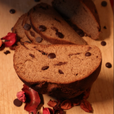 Sliced chocolate chip bread on a wooden surface with dried rose petals and chocolate chips.