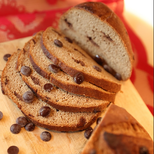 Sliced chocolate chip bread on a wooden cutting board with a red and white patterned cloth in the background.